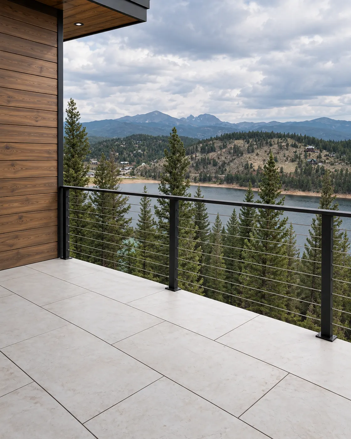 Tiled deck with a black metal cable railing, overlooking pine forest, a lake and distant mountains. Mbrico tile with Viewrail railing.